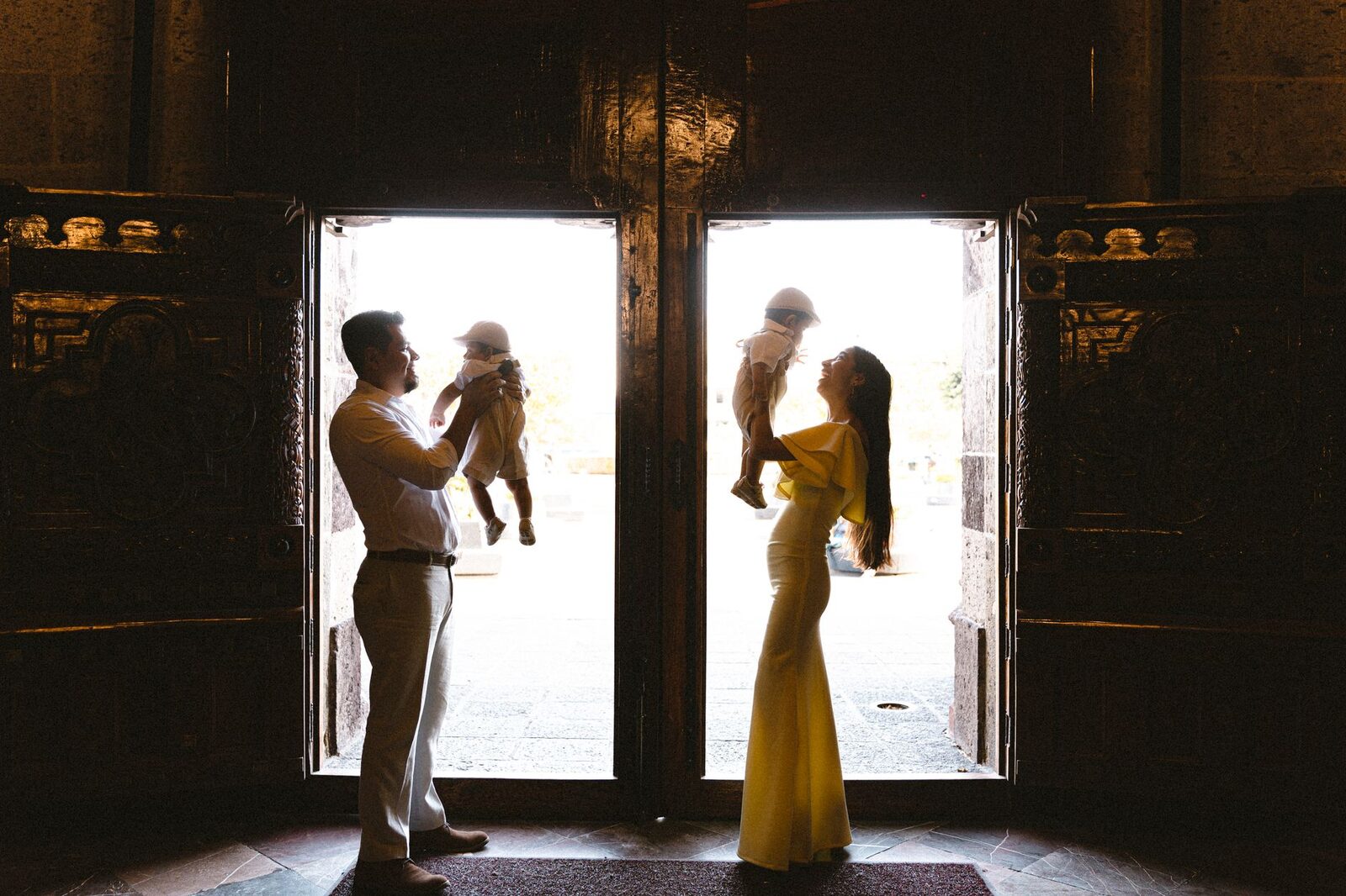 A family stands silhouetted in a doorway, each holding a baby.